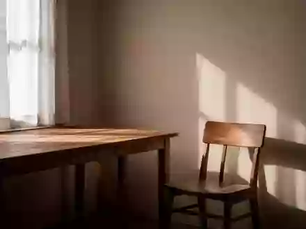 Ein ruhiger, sonnendurchfluteter Raum mit einem leeren Stuhl und einem Holztisch, der eine Atmosphäre der Stille vermittelt. - Foto: über boerse-global.de