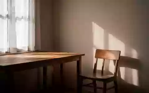 Ein ruhiger, sonnendurchfluteter Raum mit einem leeren Stuhl und einem Holztisch, der eine Atmosphäre der Stille vermittelt. - Foto: über boerse-global.de