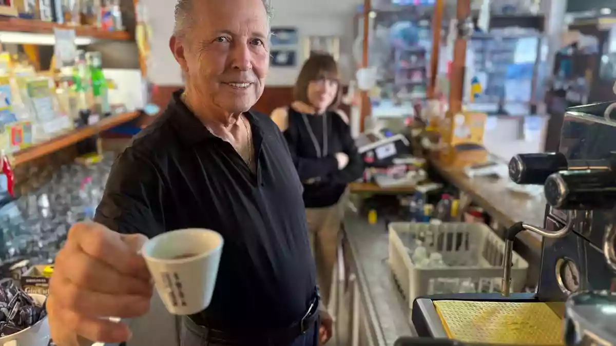 Orlando Paldino zeigt stolz eine Tasse Espresso für 70 Cent. Im Hintergrund steht seine Frau Rosina Furiati. - Bild: Christoph Sator/dpa