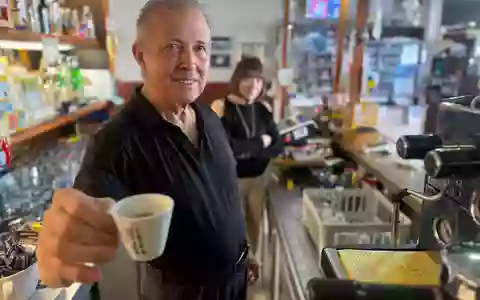 Orlando Paldino zeigt stolz eine Tasse Espresso für 70 Cent. Im Hintergrund steht seine Frau Rosina Furiati. - Foto: Christoph Sator/dpa