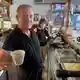 Orlando Paldino zeigt stolz eine Tasse Espresso für 70 Cent. Im Hintergrund steht seine Frau Rosina Furiati. - Bild: Christoph Sator/dpa