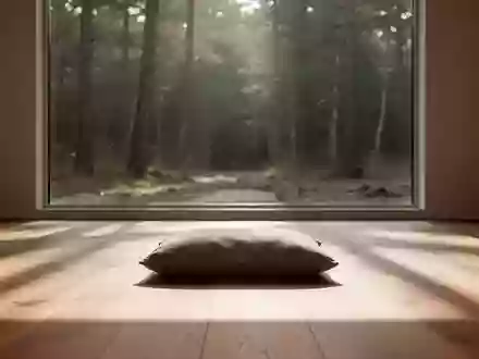 Ein minimalistischer Raum mit einem einzelnen Meditationskissen auf einem Holzboden vor einem Fenster mit Blick in den Wald. - Foto: über boerse-global.de