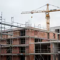 Halbfertiges Wohngebäude auf einer Baustelle mit Gerüsten und einem Baukran vor einem bewölkten Himmel. - Foto: über boerse-global.de