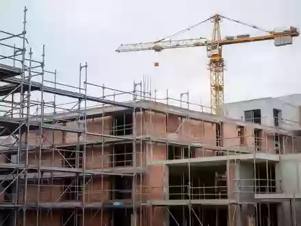 Halbfertiges Wohngebäude auf einer Baustelle mit Gerüsten und einem Baukran vor einem bewölkten Himmel. - Foto: über boerse-global.de