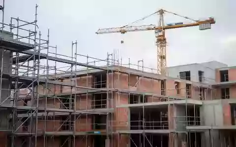 Halbfertiges Wohngebäude auf einer Baustelle mit Gerüsten und einem Baukran vor einem bewölkten Himmel. - Foto: über boerse-global.de
