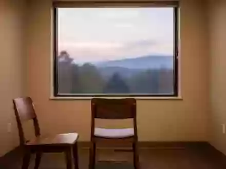 Ein minimalistischer Beratungsraum mit leerem Stuhl vor einem Fenster mit Blick auf eine Landschaft bei Dämmerung. - Foto: über boerse-global.de