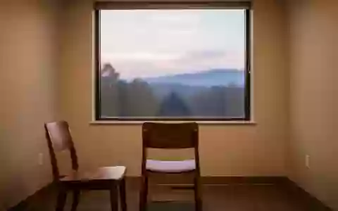 Ein minimalistischer Beratungsraum mit leerem Stuhl vor einem Fenster mit Blick auf eine Landschaft bei Dämmerung. - Foto: über boerse-global.de