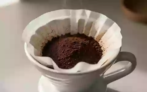 Kaffeepulver in einem Papierfilter in einem Porzellan-Kaffeefilterhalter bei natürlichem Licht. - Foto: über boerse-global.de