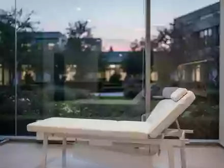 Ein minimalistischer Behandlungsraum in einer Klinik mit einer Untersuchungsliege und Blick in einen ruhigen Garten. - Foto: über boerse-global.de