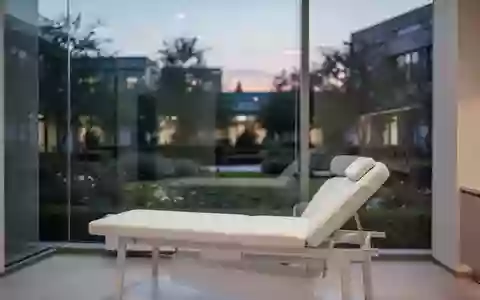 Ein minimalistischer Behandlungsraum in einer Klinik mit einer Untersuchungsliege und Blick in einen ruhigen Garten. - Foto: über boerse-global.de