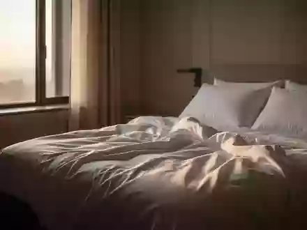 Ein minimalistisch eingerichtetes Schlafzimmer am frühen Morgen mit einfallendem Tageslicht auf einem ungemachten Bett. - Foto: über boerse-global.de