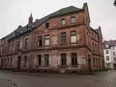 Ein historisches Backsteingebäude in einer ruhigen Stadtstraße bei bewölktem Himmel. - Foto: über boerse-global.de