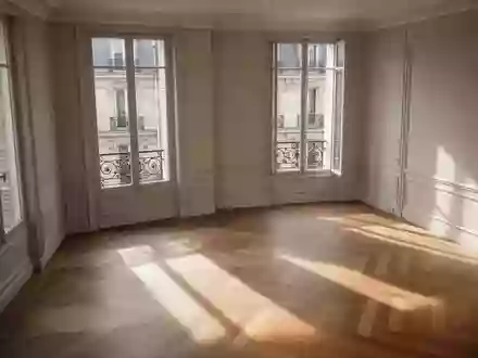 Ein minimalistisch eingerichteter, leerer Wohnraum in einer Pariser Wohnung mit Fischgrätparkett und großen Fenstern bei Tageslicht. - Foto: über boerse-global.de