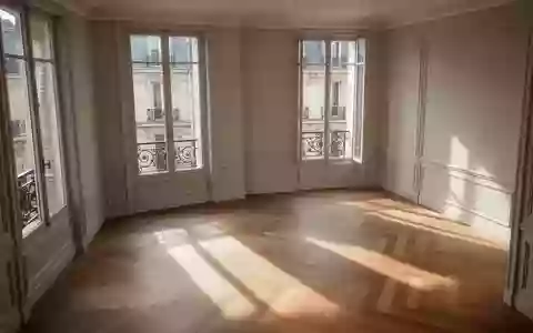 Ein minimalistisch eingerichteter, leerer Wohnraum in einer Pariser Wohnung mit Fischgrätparkett und großen Fenstern bei Tageslicht. - Foto: über boerse-global.de