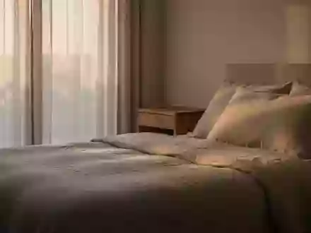 Ein minimalistisch eingerichtetes, ruhiges Schlafzimmer bei sanftem Tageslicht mit Fokus auf Textilien und Holzmöbeln. - Foto: über boerse-global.de