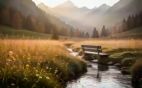 Eine ruhige Bergwiese im goldenen Licht mit einer hölzernen Bank an einem kleinen Bachlauf. - Foto: über boerse-global.de
