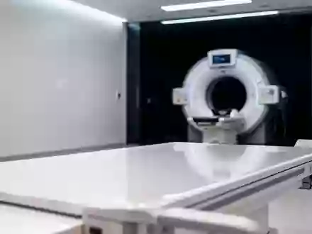 Ein steriler, minimalistischer Untersuchungsraum in einer medizinischen Einrichtung mit einem diagnostischen Bildgebungsgerät im Hintergrund. - Foto: über boerse-global.de