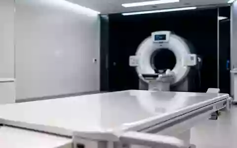 Ein steriler, minimalistischer Untersuchungsraum in einer medizinischen Einrichtung mit einem diagnostischen Bildgebungsgerät im Hintergrund. - Foto: über boerse-global.de