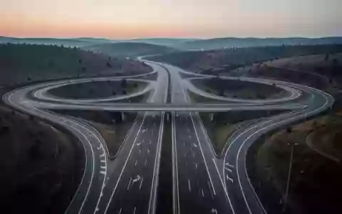 Eine weitläufige, moderne Autobahnkreuzung in der Dämmerung, umgeben von einer ruhigen Hügellandschaft. - Foto: über boerse-global.de