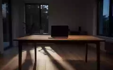 Ein leerer Schreibtisch mit einem zugeklappten Laptop in einem schlichten, abgedunkelten Raum mit einfallendem Tageslicht. - Foto: über boerse-global.de