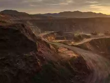 Ein offenes Bergbaugelände bei Sonnenuntergang mit Erdhügeln und Baumaschinen im Hintergrund. - Foto: über boerse-global.de
