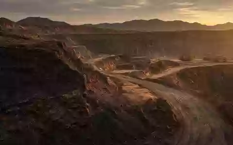 Ein offenes Bergbaugelände bei Sonnenuntergang mit Erdhügeln und Baumaschinen im Hintergrund. - Foto: über boerse-global.de