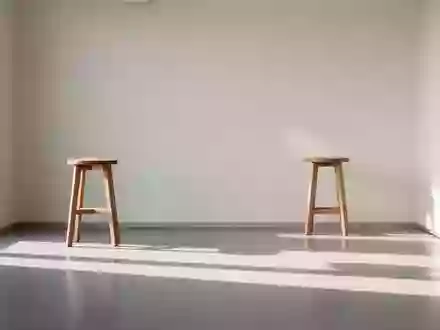 Ein minimalistischer, heller Untersuchungsraum in einer medizinischen Praxis mit einem leeren Holzschemel vor einer Wand. - Foto: über boerse-global.de