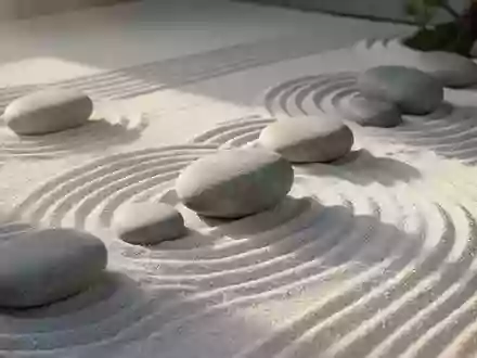 Ein minimalistischer Zen-Garten mit glatten Flusskieselsteinen auf geharktem Sand bei sanftem Morgenlicht. - Foto: über boerse-global.de
