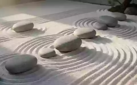 Ein minimalistischer Zen-Garten mit glatten Flusskieselsteinen auf geharktem Sand bei sanftem Morgenlicht. - Foto: über boerse-global.de