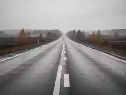 Eine leere, nasse Landstraße, die sich in einer trüben Herbstlandschaft bis zum Horizont erstreckt. - Foto: über boerse-global.de