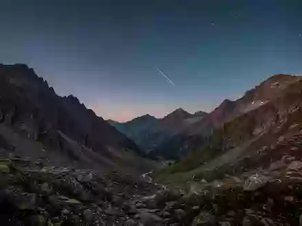 Eine weitläufige Berglandschaft bei Dämmerung mit klarem Sternenhimmel und der Andeutung eines Satelliten am Horizont. - Foto: über boerse-global.de