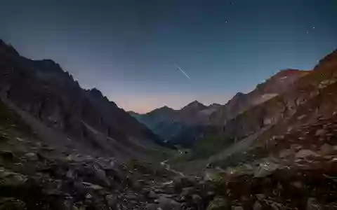 Eine weitläufige Berglandschaft bei Dämmerung mit klarem Sternenhimmel und der Andeutung eines Satelliten am Horizont. - Foto: über boerse-global.de