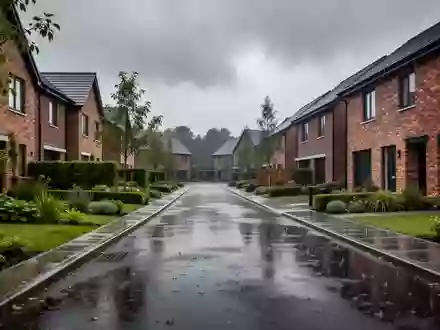 Eine ruhige Wohnstraße nach einem starken Regen mit nassen Straßen und Häuserfassaden unter einem bewölkten Himmel. - Foto: über boerse-global.de