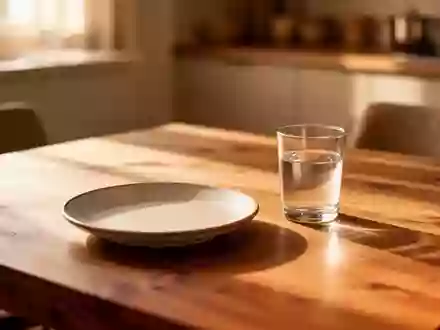 Ein schlichter, leerer Essteller und ein Glas Wasser auf einem Holztisch in warmem, natürlichem Nachmittagslicht. - Foto: über boerse-global.de