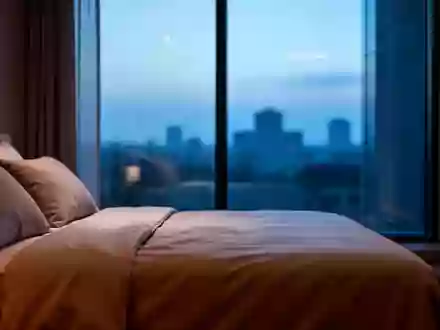 Ein minimalistisch eingerichtetes Schlafzimmer in den frühen Morgenstunden mit Blick auf eine ruhige, städtische Kulisse. - Foto: über boerse-global.de