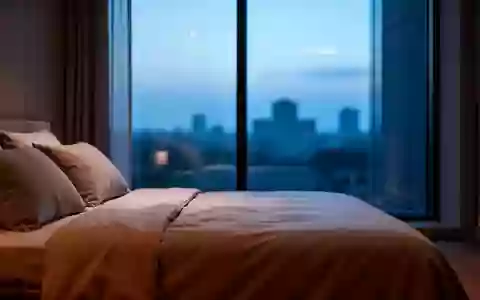 Ein minimalistisch eingerichtetes Schlafzimmer in den frühen Morgenstunden mit Blick auf eine ruhige, städtische Kulisse. - Foto: über boerse-global.de