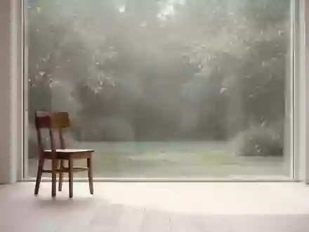 Ein minimalistisch eingerichteter, lichtdurchfluteter Raum mit einem leeren Holzstuhl und Blick in einen ruhigen Garten. - Foto: ĂĽber boerse-global.de