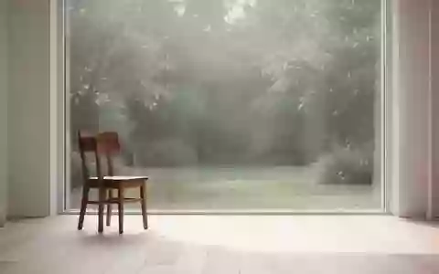 Ein minimalistisch eingerichteter, lichtdurchfluteter Raum mit einem leeren Holzstuhl und Blick in einen ruhigen Garten. - Foto: über boerse-global.de