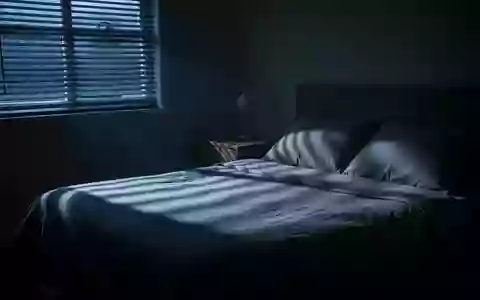 Ein ruhiges, abgedunkeltes Schlafzimmer im Morgengrauen mit sanftem Lichteinfall und langen Schatten auf dem unberührten Bett. - Foto: über boerse-global.de