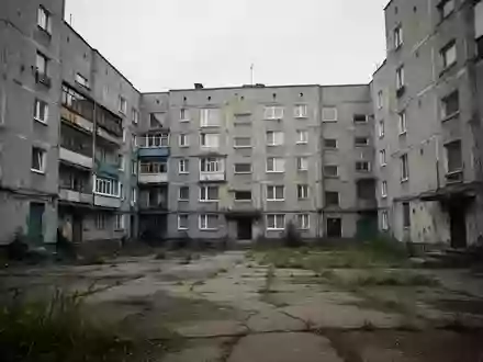 Ein grauer, sanierungsbedürftiger Plattenbau in einer Wohnsiedlung bei bewölktem Himmel. - Foto: über boerse-global.de