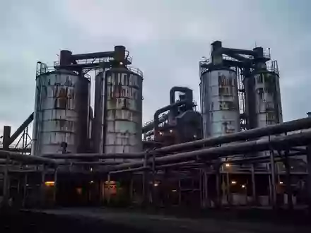 Industrielle Industrieanlage mit groĂen Metallsilos und Rohrleitungen vor einem bewölkten Abendhimmel. - Foto: ĂŒber boerse-global.de