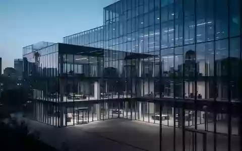 Ein modernes, minimalistisches Bürogebäude aus Glas in der Dämmerung, das die Lichter der Stadt reflektiert. - Foto: über boerse-global.de