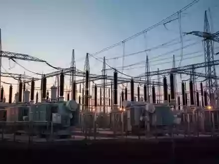 Eine weitläufige elektrische Umspannstation mit Hochspannungstransformatoren und Stromleitungen in der Abenddämmerung. - Foto: über boerse-global.de