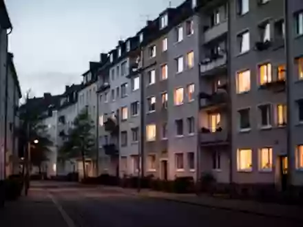Eine ruhige Wohnstraße in einer deutschen Stadt bei Dämmerung mit beleuchteten Fenstern eines Mehrfamilienhauses. - Foto: über boerse-global.de