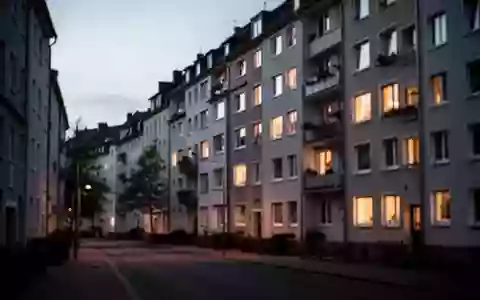 Eine ruhige Wohnstraße in einer deutschen Stadt bei Dämmerung mit beleuchteten Fenstern eines Mehrfamilienhauses. - Foto: über boerse-global.de