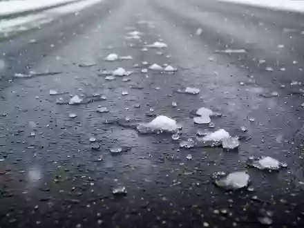 Dunkler Asphalt auf einer Straße bei leichtem Schneefall mit einzelnen Schneeresten und Eis auf der Fahrbahn. - Foto: über boerse-global.de