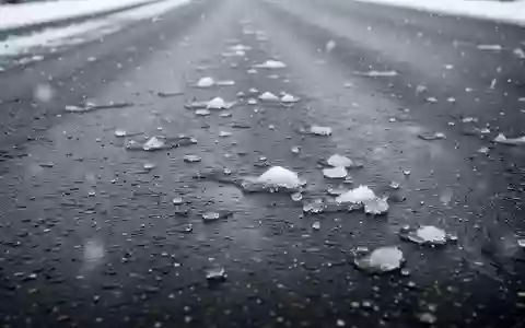 Dunkler Asphalt auf einer Straße bei leichtem Schneefall mit einzelnen Schneeresten und Eis auf der Fahrbahn. - Foto: über boerse-global.de