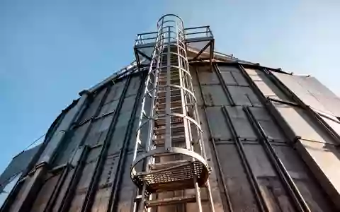 Metallene Aufstiegsleiter mit Rückenschutz an einem hohen landwirtschaftlichen Silo aus Beton. - Foto: über boerse-global.de