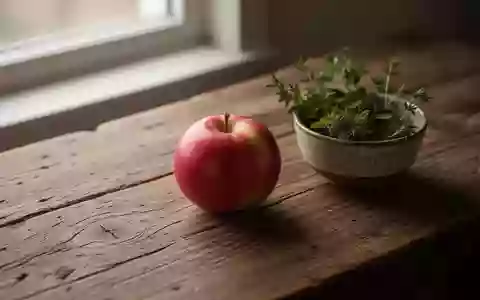 Ein einzelnes Stück reifes Obst und eine Schale mit Kräutern auf einem rustikalen Holztisch im sanften Tageslicht. - Foto: über boerse-global.de