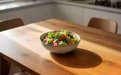 Eine schlichte Schale mit frischem Salat auf einem hölzernen Esstisch in einem hellen, sonnendurchfluteten Raum. - Foto: über boerse-global.de